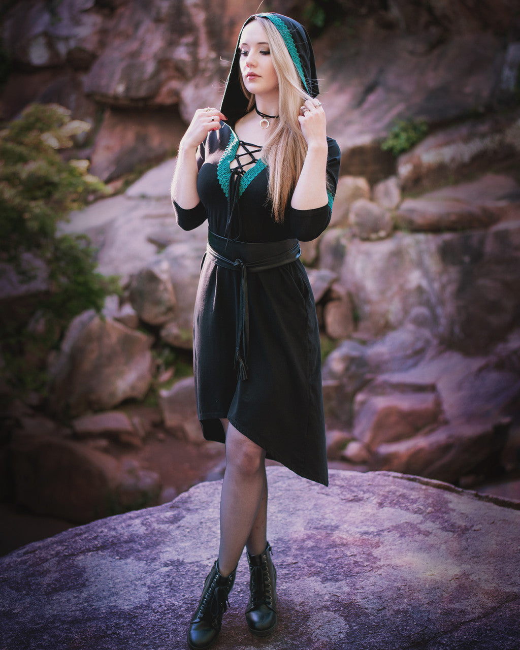 Woman posing on rocks, showing side view of the Dahlia Hooded Dress wearing oversized hood paired with tights.