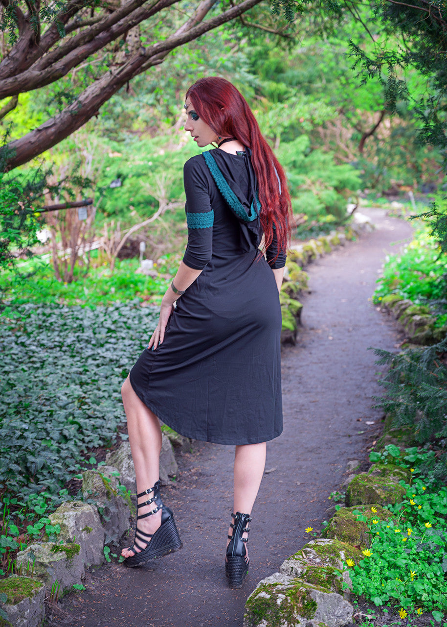 Woman posing showing oversized hood on the Dahlia Hooded Dress surrounded by trees.