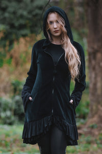 Model posing in woods, showing front view of Occultist Coat hands partial in both outer pockets.