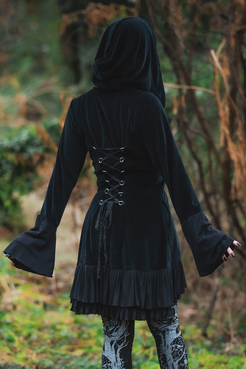 Model posing in woods, showing adjustable lace up back, large wide hood, and draping cuffs of the Occultist Coat.