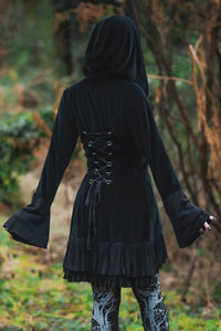 Model posing in woods, showing adjustable lace up back, large wide hood, and draping cuffs of the Occultist Coat.