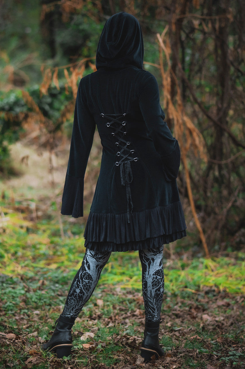 Model posing in woods showing back view of Occultist Coat highlighting adjustable lace up back with d-rings.