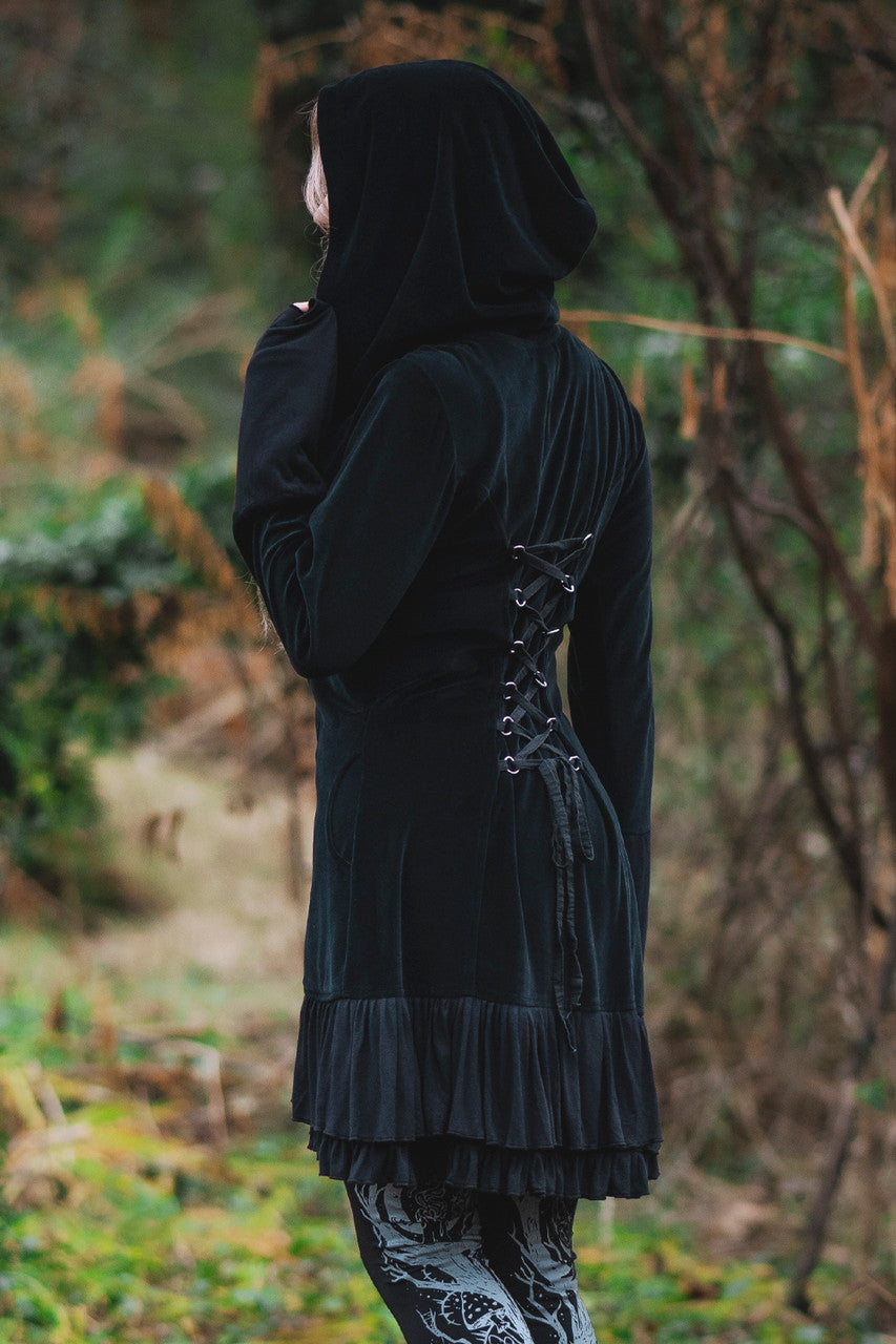 Model posing in woods, showing adjustable lace up back of the Occultist Coat and large wide hood.