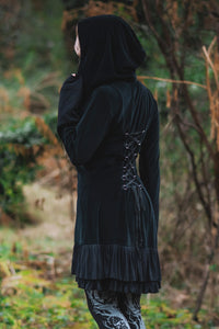 Model posing in woods, showing adjustable lace up back of the Occultist Coat and large wide hood.